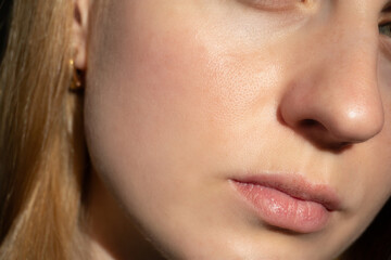 Obraz premium Close-up of a young woman’s face with clean, smooth skin and visible pores. Natural lighting highlights healthy texture, minimal redness, and authentic beauty details.