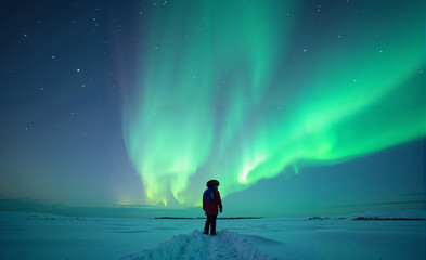 A child standing alone in a field of snow, gazing up at the northern lights