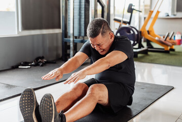 Southeast Asian middle-aged man tries to touch his toes while seated, showing discomfort during...