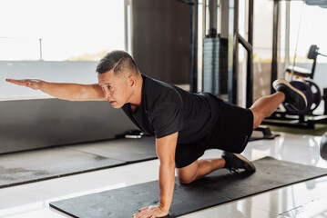 Southeast Asian man in his 50s balances in bird dog pose on a mat, focusing on core strength and...