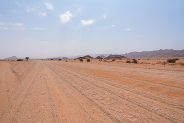 Obraz premium Sandpiste als Strasse quer durch die weiten Wüsten von Namibia im Namib Gebiet