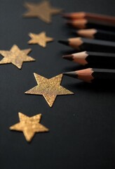 Closeup of Gold and Black Stars with Pencils on Dark Surface.