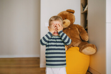 Adorable toddler playing peek-a-boo indoors