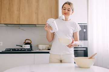 Woman using a hand mixer to prepare ingredients in modern kitchen