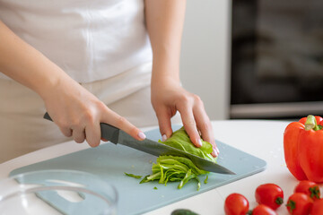 Woman chopping fresh vegetables on a cutting board in a home kitchen