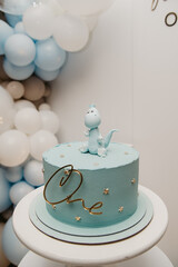 cake covered with blue mastic with a decorative figure on it and the inscription number one, standing on a stand on an isolated background for a birthday celebration