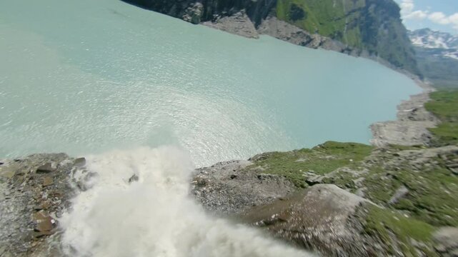Stunning FPV and drone shots soaring through the Swiss Alps, capturing the Mauvoisin Dam and its majestic waterfall on a clear, sunny summer day.