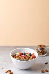 Vertical photo of a white bowl with kefir, fruits and granola on light grey surface, with solid peach background and negative space at the top. Concept of healthy eating and minimalist aesthetics