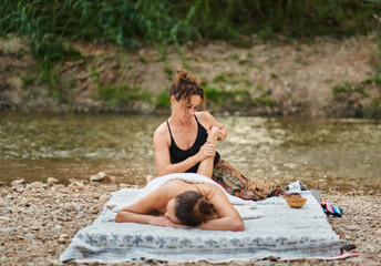 Massage therapist performing leg massage by the river, wellness and relaxation