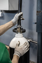 Close-up of gloved hands attaching a black and white gas cylinder to a pipe system in an industrial...