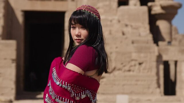 A woman in a red outfit dances near ancient ruins in Dendera, Egypt