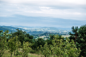 Obraz premium Panoramic view of a rural valley with scattered houses and rolling hills under a cloudy sky. Agricultural landscape, rural development, land use, countryside sustainability..