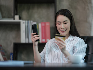 Portrait of an Asian businesswoman holding a credit card and using a smartphone for shopping online.