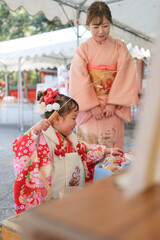Obraz premium On a sunny spring day at a shrine, a Japanese woman in her thirties and her 3-year-old daughter in kimonos celebrate Shichi-Go-San. They draw omikuji, sharing a joyful moment in a peaceful setting.