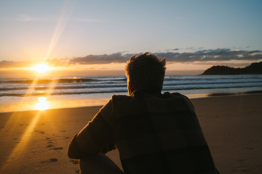 Man squats on Manly Beach watching the golden sunrise