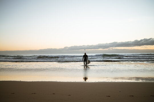 Surfer walks into ocean at sunrise on Manly Beach, Australia