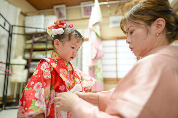 Obraz premium A Japanese couple in their thirties, in pink kimonos, help their 3-year-old daughter into her kimono for Shichi-Go-San. This photo captures family love and care before a traditional celebration.