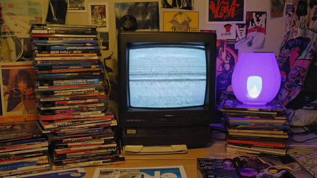 small vintage tv with No Signal screen between stacked CDs with lamp and posters on wall