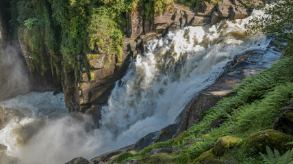 A panoramic wallpaper of a roaring waterfall cascading down the rocks surrounded by lush greenery