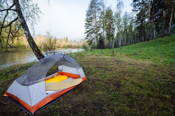 Experience a serene campsite by the river, where a cozy tent is nestled amidst the stunning natural...