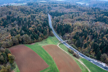 Highway Construction Site Stretching Through Farmland, Forest, and Distant Village Captured by Drone Under Overcast Sky
