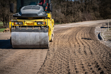 Generated ImageLow Angle Shot of Compact Roller on Road Construction Site Surrounded by Trees and Clear Blue Sky on Sunny Day

