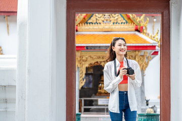 Young Asian woman traveling backpacker walking in temple at Bangkok Thailand. Happy female tourist walking in the downtown street traditional ancient temple. Holiday vacation time tourist