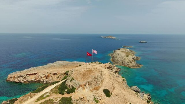 Smooth aerial view of Zafer Burnu in Northern Cyprus with national flags on a cliffside, blending sea, landscape, and symbolism in 50fps clarity.