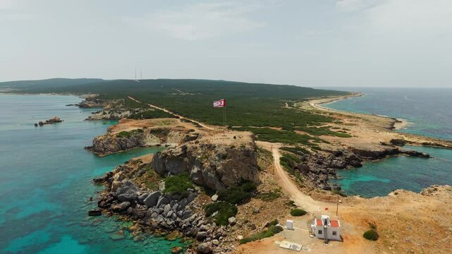 Aerial drone shot of Zafer Burnu in Northern Cyprus with Turkish and TRNC flags on a rocky cliff above the Mediterranean Sea, filmed in 50 frames per second.