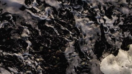 Foamy waves crash over black pebbles and melting ice on Iceland’s Diamond Beach - Powered by Adobe