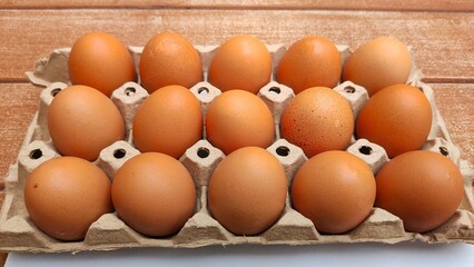 A carton of fifteen brown eggs arranged neatly on a wooden surface.