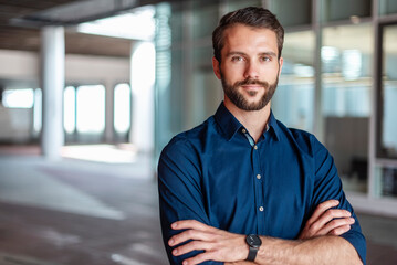 Confident businessman in blue shirt standing with arms crossed in a modern office