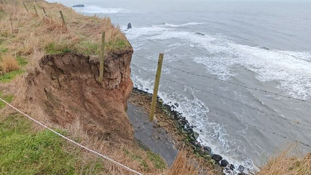 Barbed wire fence hanging on the edge of a steep cliff after a landslide on the English coa