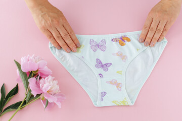 Women's hands with a white panties on the pink background.