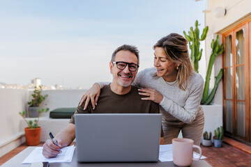 Couple working on a laptop at home on a sunny rooftop terrace