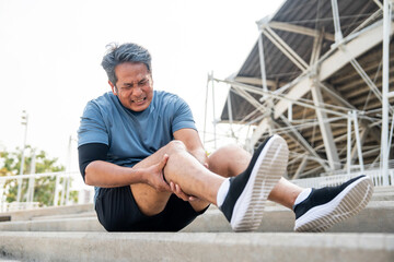 Mature man tired and leg pain during jogging at sport stadium. Runner has sore knees because he has...