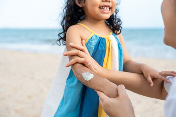 Asian mom applying sunscreen to her happy child’s face on the beach for skin protection from the sun. a young mother carefully smears protective cream on her daughter’s face for safe outdoor fun.