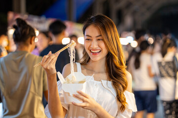 Asian woman enjoy eating noodles street food at night market. Traveler Asian blogger women Happy tourists Beautiful female with Traditional thailand bangkok food.