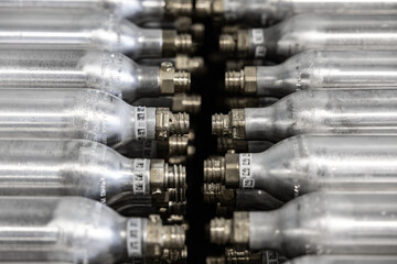 Neatly arranged silver gas cylinders with brass valves and engraved markings, displayed in an...