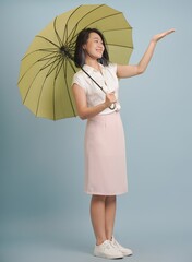 Young woman holding a green umbrella while smiling against a blue background in a casual studio...