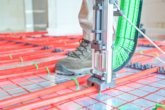 A technician skillfully installs an underfloor heating system using advanced technology, showcasing precise placement and modern plumbing techniques in a construction setting