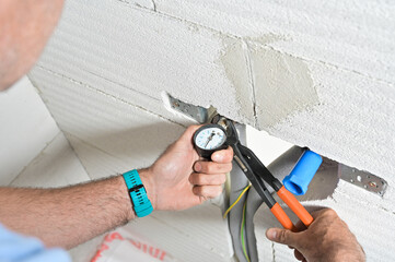 A technician is using a pressure gauge and pliers to inspect plumbing work on a wall, showcasing practical home maintenance skills and service tools being used