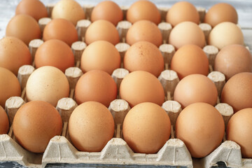 Brown chicken eggs in a cardboard tray on a rustic wood background for farm and food concepts and healthy eating or cooking recipes and ingredients advertising.