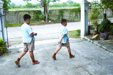 Two siblings in school uniforms walk to school.