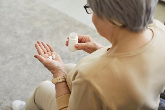 Back view of middle aged woman holding bottle of drugs, taking medicine prescribed by doctor, complex supplements, vitamins, taking care of her health, being at home, managing chronic pain - Powered by Adobe