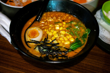 A bowl of miso ramen, possibly corn butter ramen, featuring a halved boiled egg, corn, and seaweed,...