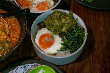 A bowl of rice with side dishes, likely dhal, green vegetables, and a boiled egg, arranged on a wooden table, creating a simple yet appetizing meal