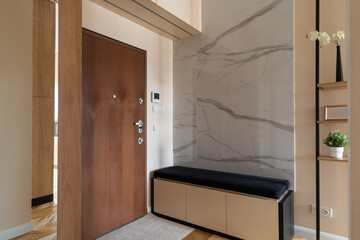 Apartment entryway: wooden door, marble accent wall, and storage bench. This modern hall has shelves with plants for a welcoming, elegant ambiance. Stylish residential interior. Functional design.