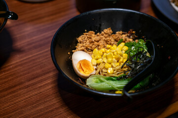 A vibrant bowl of dry ramen (mazesoba), a popular noodle dish, topped with minced meat, corn, green onions, seaweed, and a perfectly halved egg, on a wooden table.