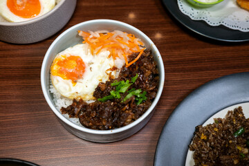 A bowl of rice with side dishes, likely dhal, green vegetables, and a boiled egg, arranged on a wooden table, creating a simple yet appetizing meal